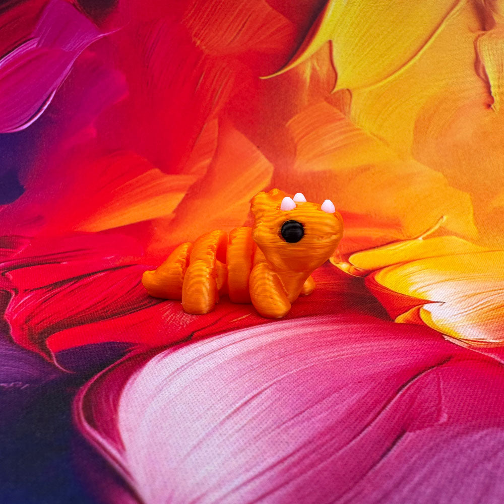Small orange toy lizard on a colorful flower with vibrant pink, yellow, and red petals.